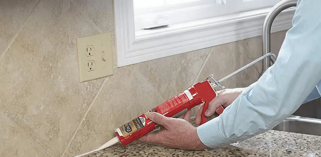 Handyman applying caulk along a kitchen backsplash and countertop seam in Birmingham, AL